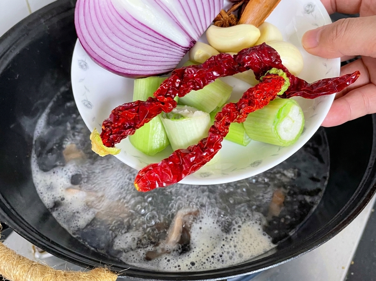 Costine di maiale in un wok con aromi e acqua bollente versata sopra.