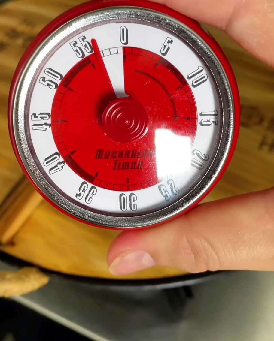 Un timer da cucina impostato su unora con una pentola in ebollizione sullo sfondo.