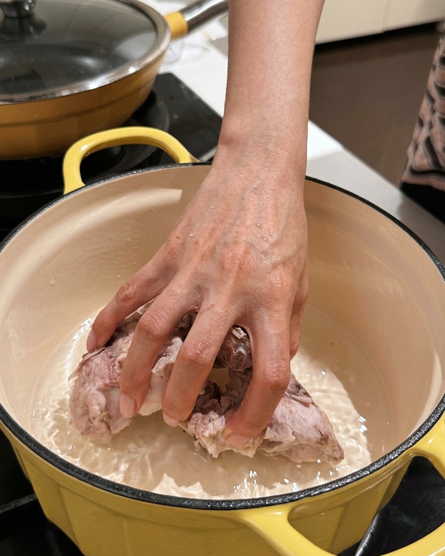 Una mano che rimette i pezzi di spina di maiale puliti in una pentola pulita per brasatura.
