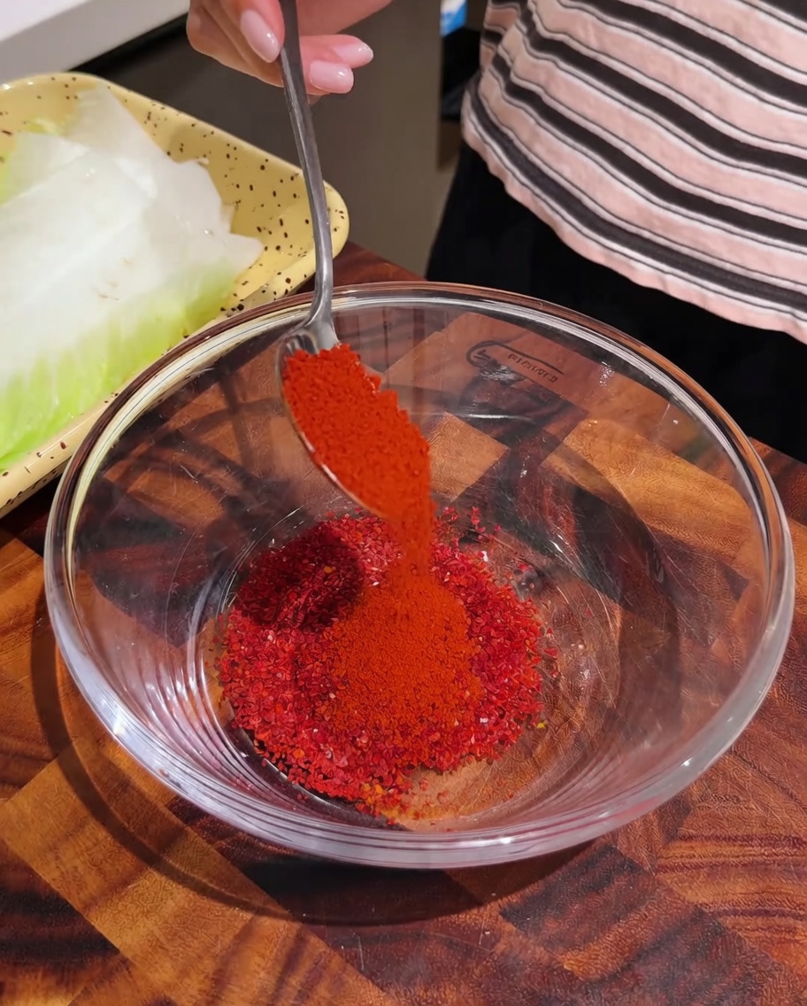Peperoncino rosso in polvere versato con un cucchiaio in una ciotola di vetro trasparente contenente altre spezie.