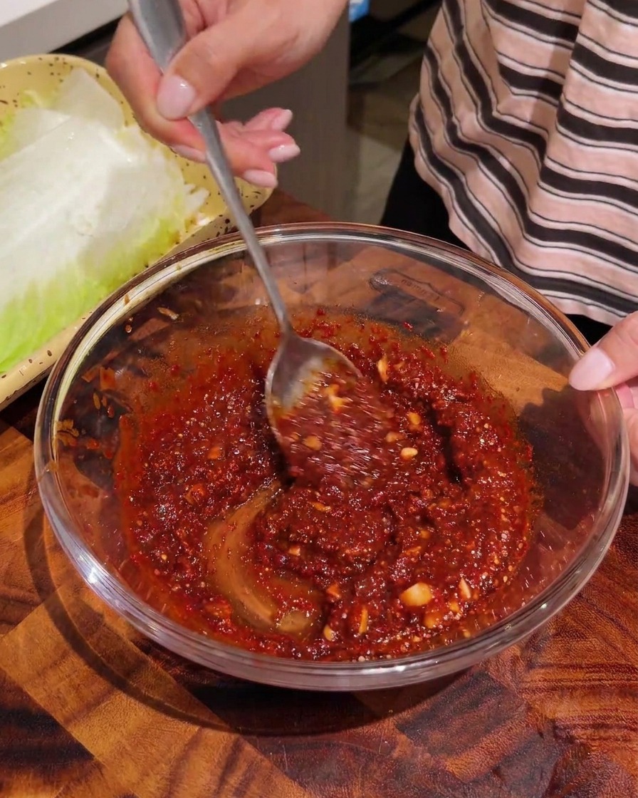Strisce strappate di cavolo cinese sbollentato mescolate con una salsa di condimento rossa in una ciotola di vetro.