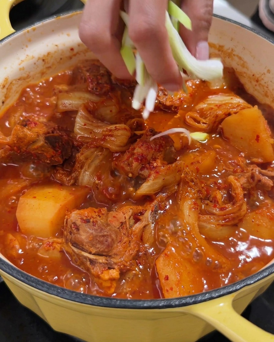 Una pentola vibrante di zuppa piccante di spine di maiale guarnita con cipollotti freschi tritati.