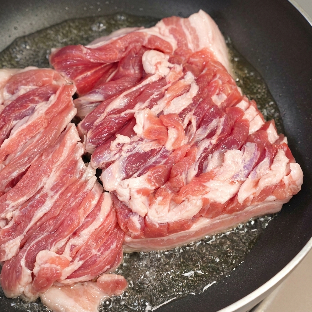 Una padella con pancetta sfrigolante e un cucchiaio che rimuove il grasso sciolto in eccesso.
