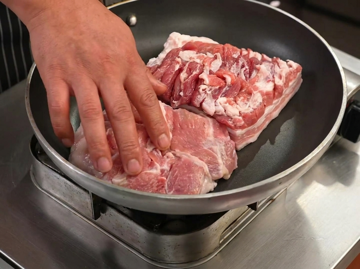 Fette di pancia di maiale che friggono in una padella asciutta, iniziando a dorarsi e a rilasciare il grasso.