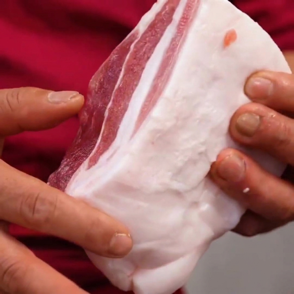 Pancetta di maiale tenuta tra le mani, che mostra i tagli a griglia fatti con un angolo di 45 gradi.