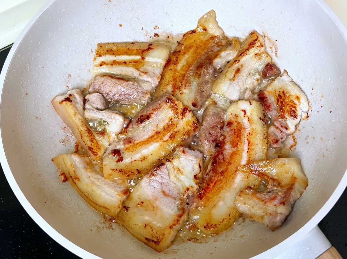 Fette di pancetta che friggono e dorano nella padella con grasso sciolto.