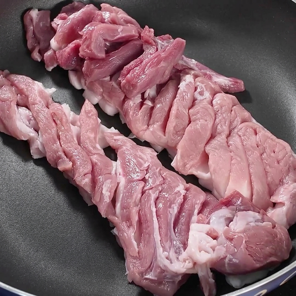 Fette di pancetta disposte ordinatamente allinterno di una padella scura sopra il fuoco del piano cottura.