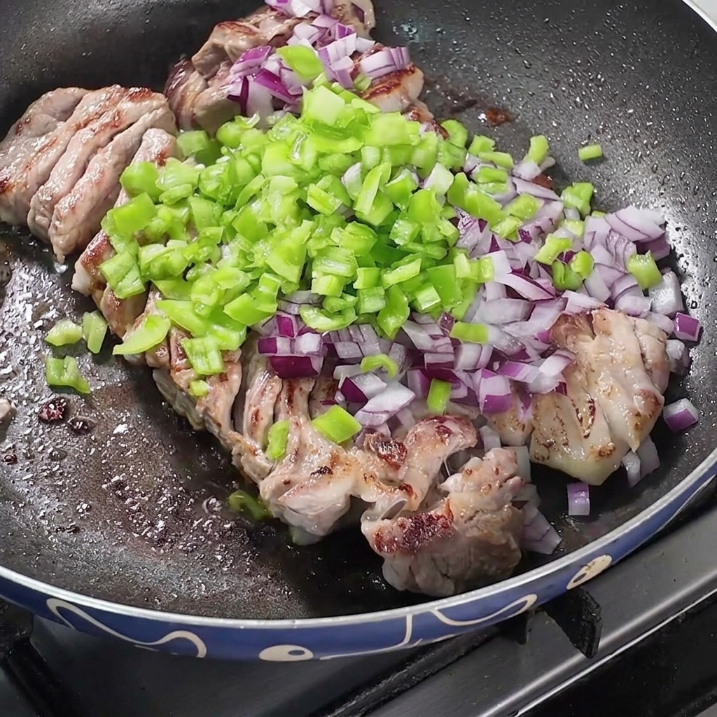 Una padella piena di pancetta in cottura sormontata da mucchietti di cipolle rosse tritate, peperoni verdi e spezie secche.