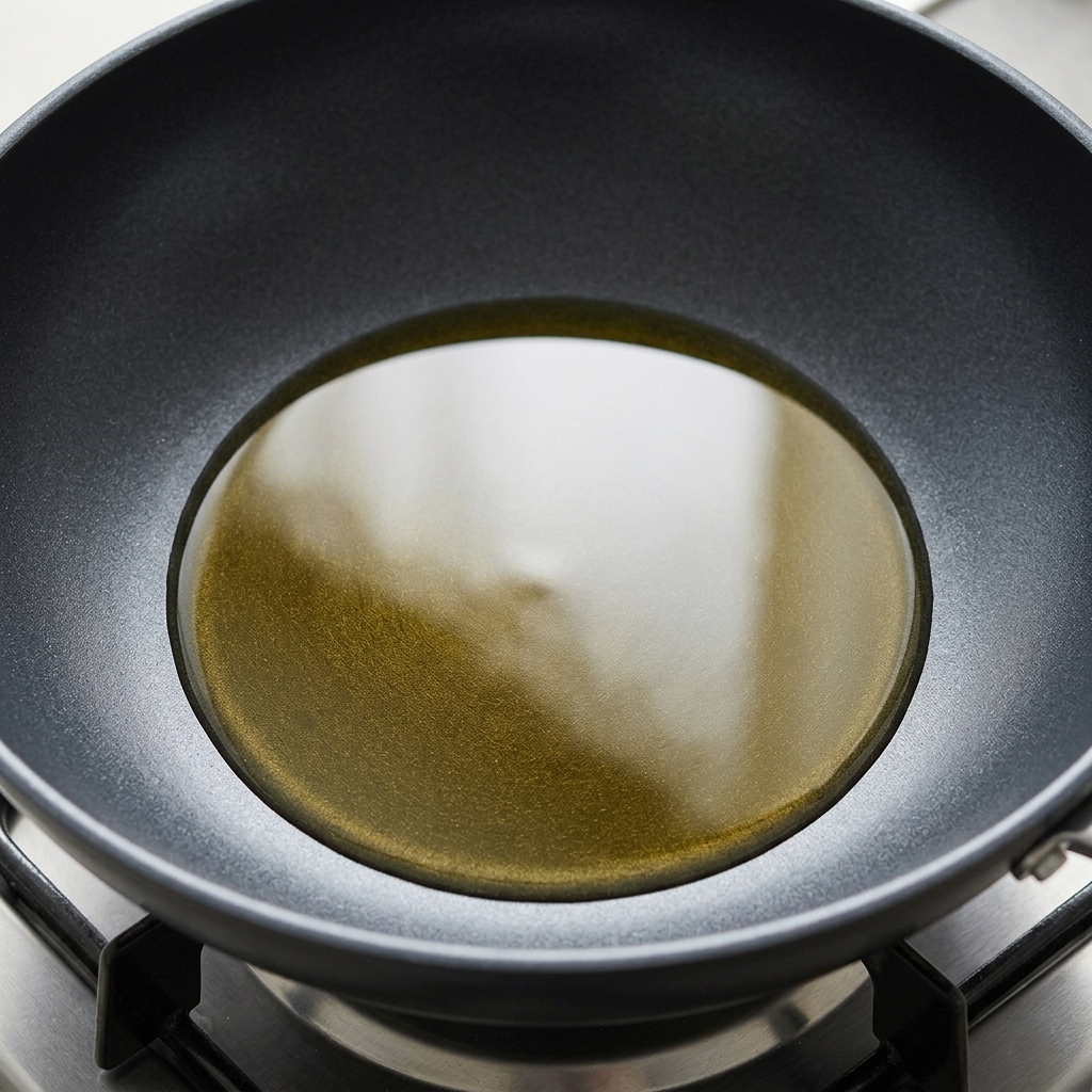 Olio da cucina dorato che frigge allinterno di una padella scura poggiata sul fornello a gas.