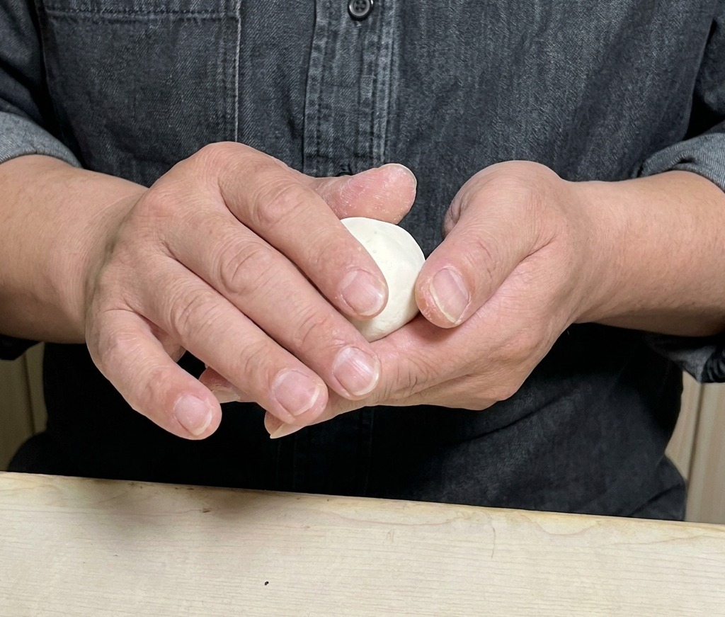 Mani che piegano e sigillano con cura un involucro di pasta rotondo riempito con il composto di carne.