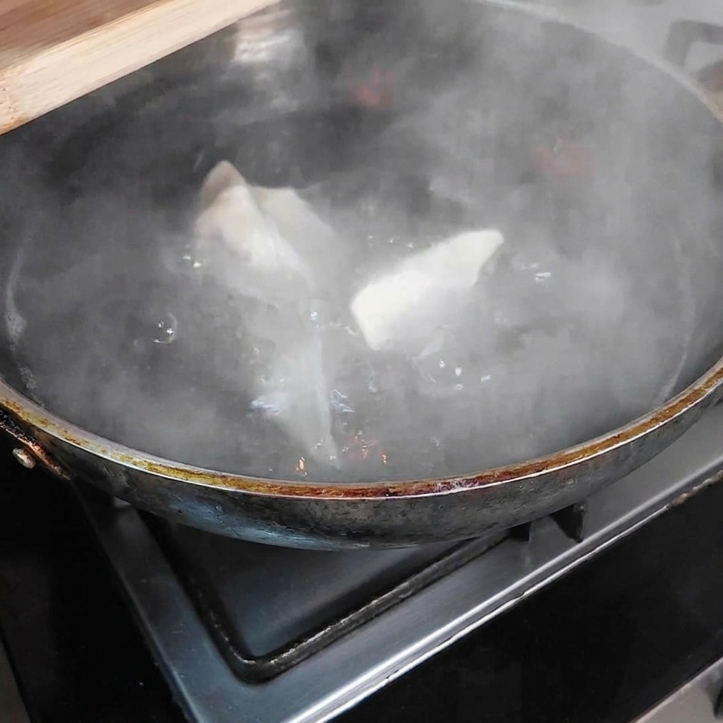Diversi ravioli immersi in una grande pentola di acqua bollente, con vapore che sale dalla pentola.