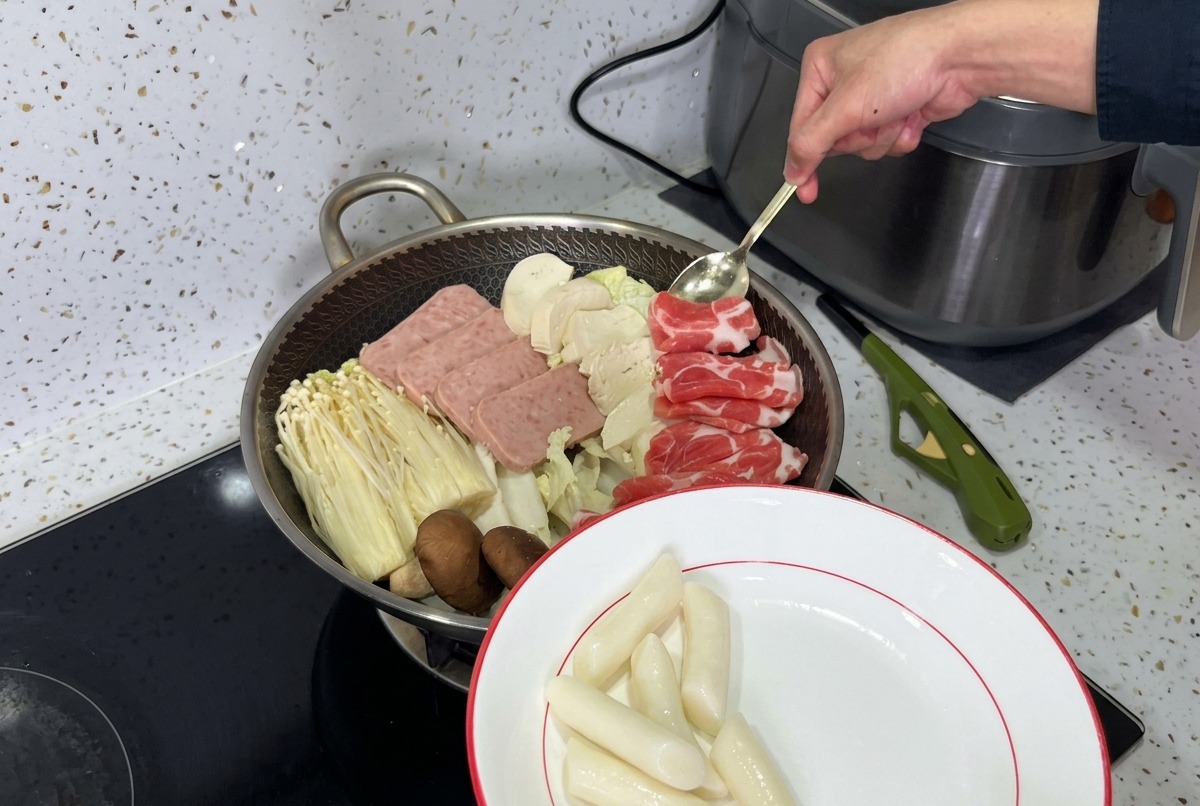 Una pentola splendidamente disposta di stufato militare coreano, con strati di carne in scatola, funghi, tofu e kimchi fresco pronti per il brodo.