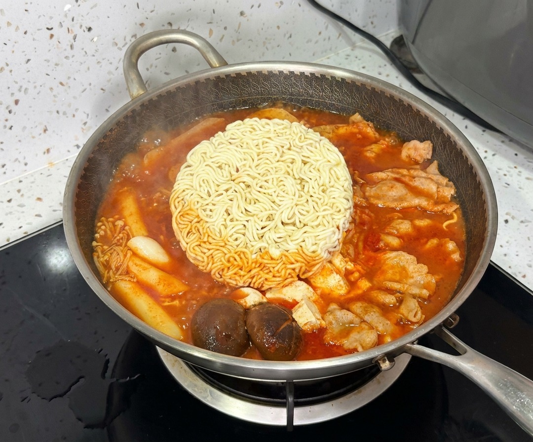 Un blocco di noodles ramen che cuoce al centro del vivace e bollente stufato militare coreano.