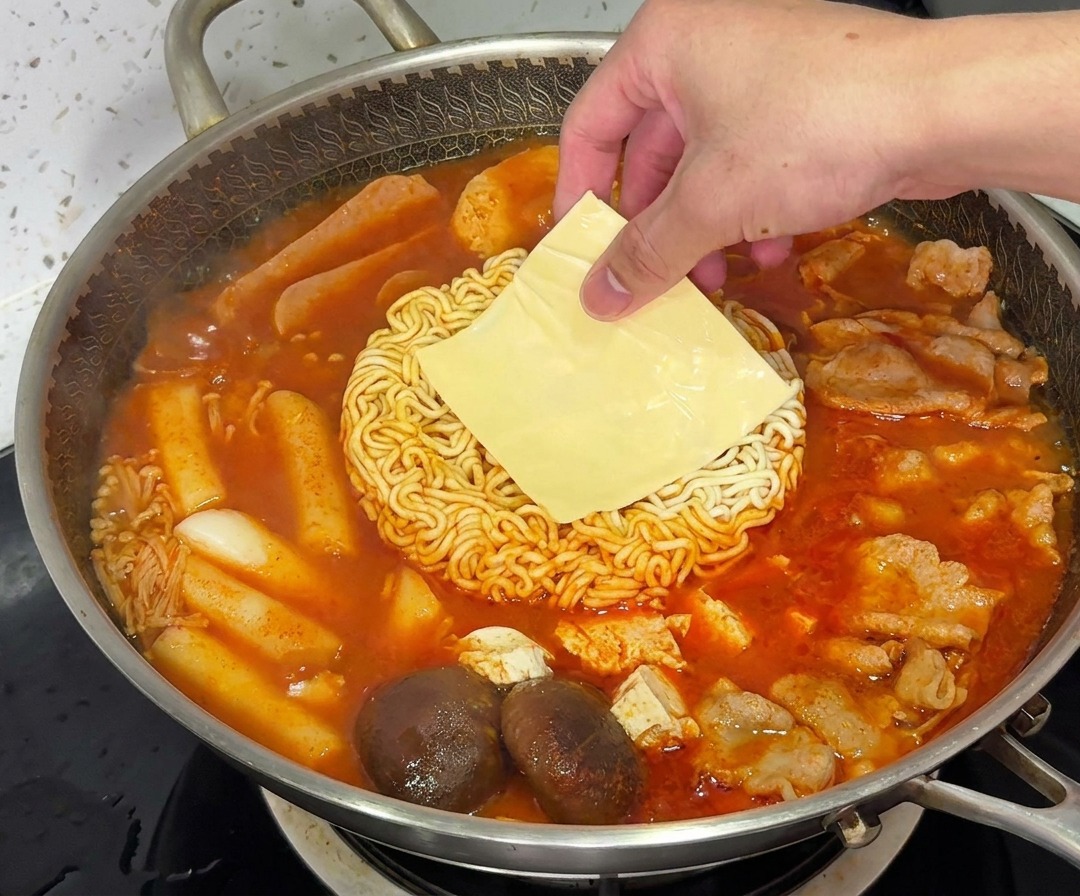 Una fetta di formaggio giallo che si scioglie sopra i noodles ramen in una pentola fumante di Budae Jjigae.