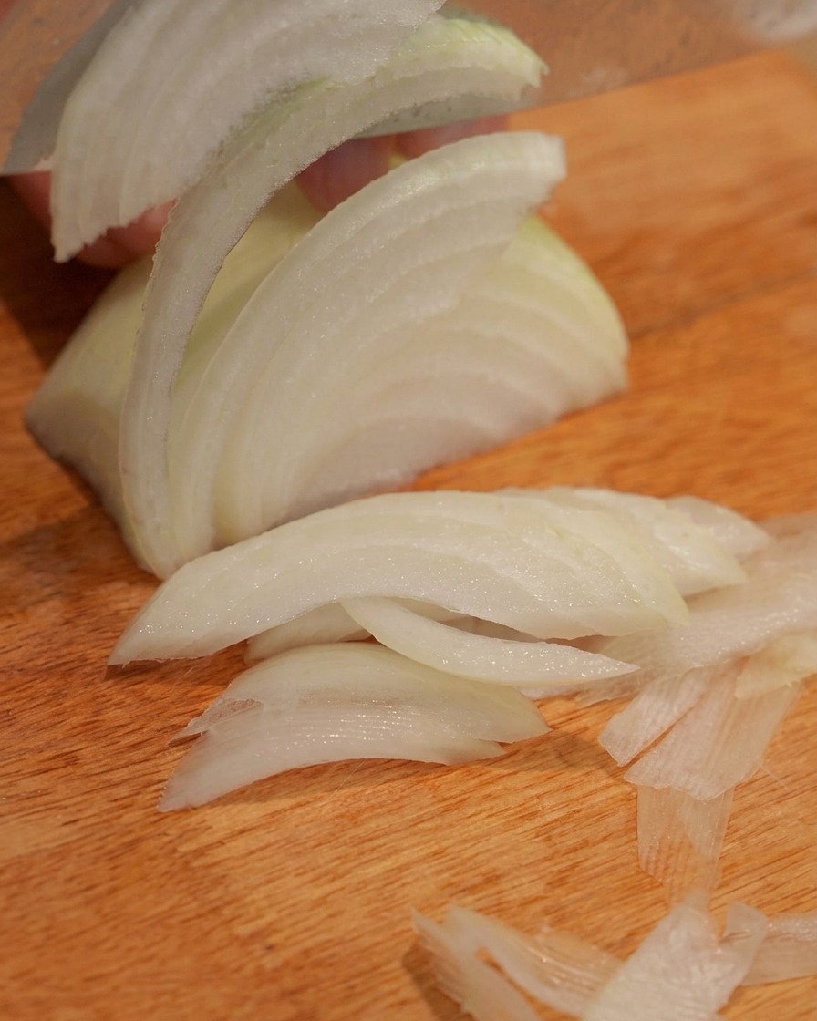 Una cipolla tagliata a strisce su un tagliere di legno.