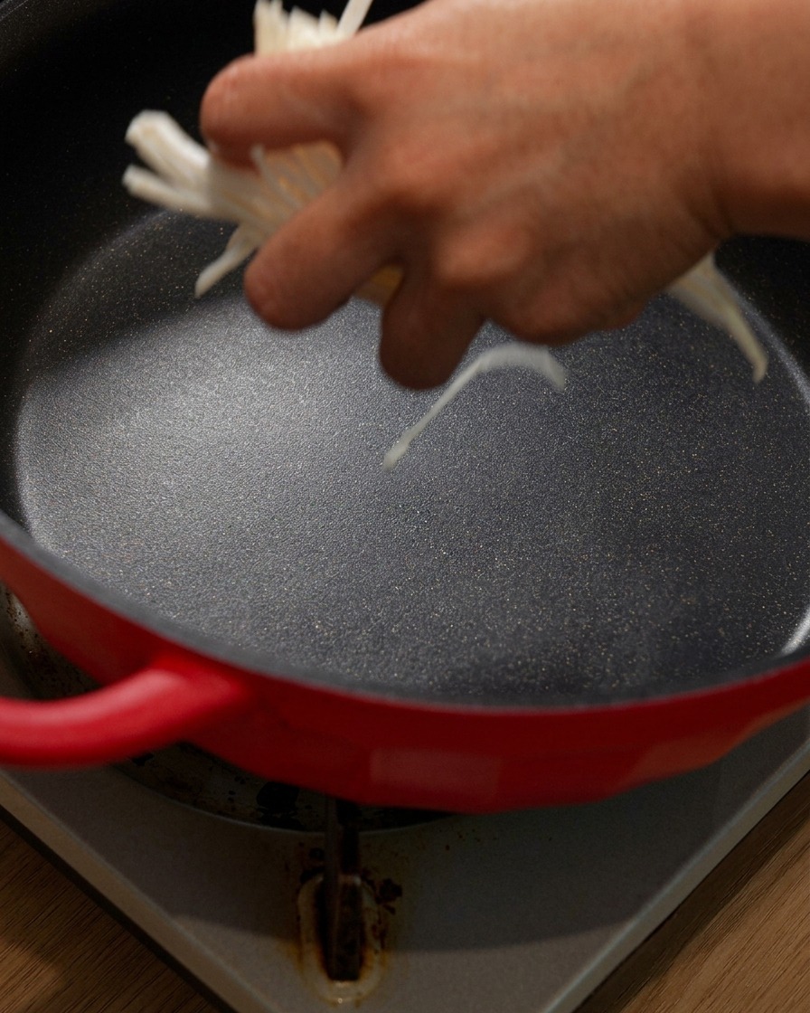 Cipolle affettate aggiunte sul fondo di una pentola rossa.