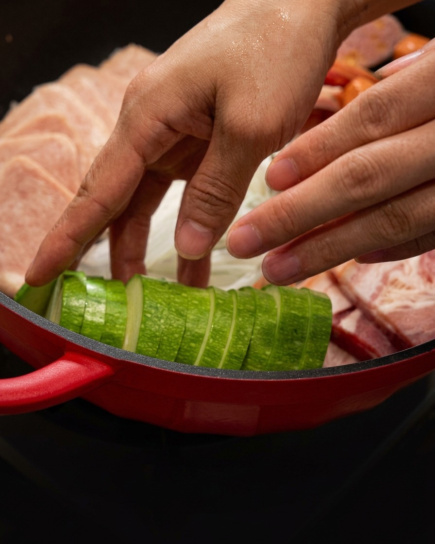Fette di zucchina posizionate ordinatamente nella pentola rossa insieme alla carne.
