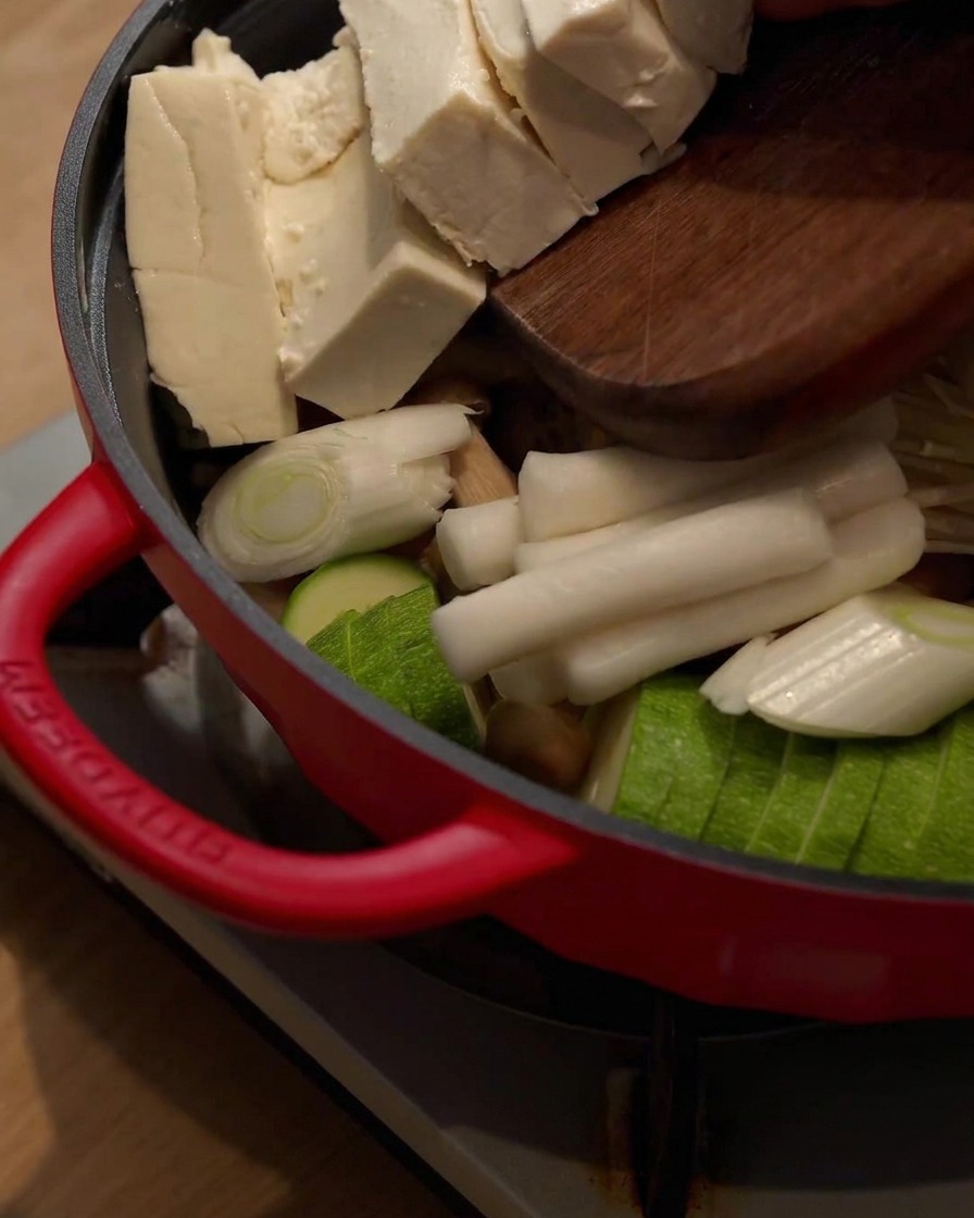 Blocchi di tofu fatti scivolare da un tagliere di legno nellhot pot contenente altri ingredienti.