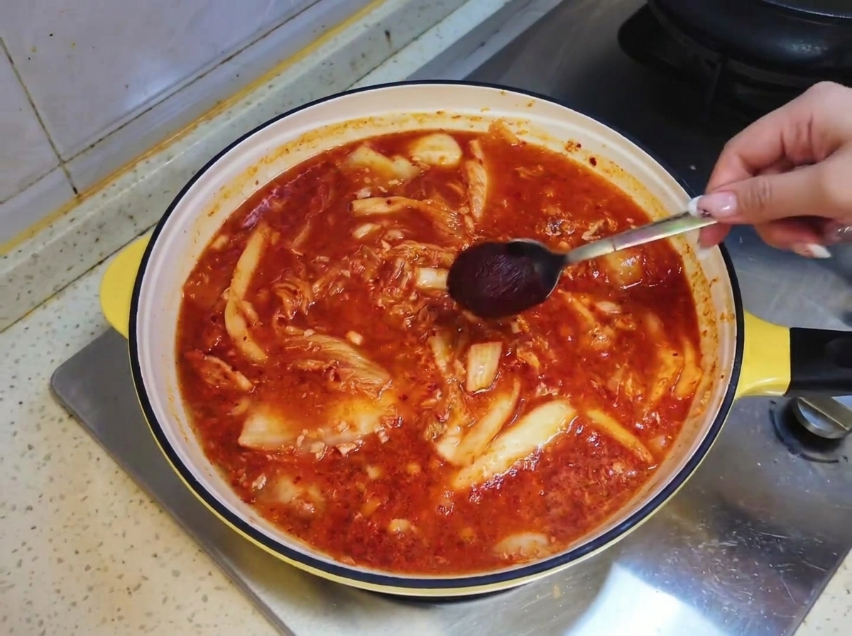 Un cucchiaio di salsa piccante coreana immerso nel brodo rossastro della zuppa allinterno della padella.
