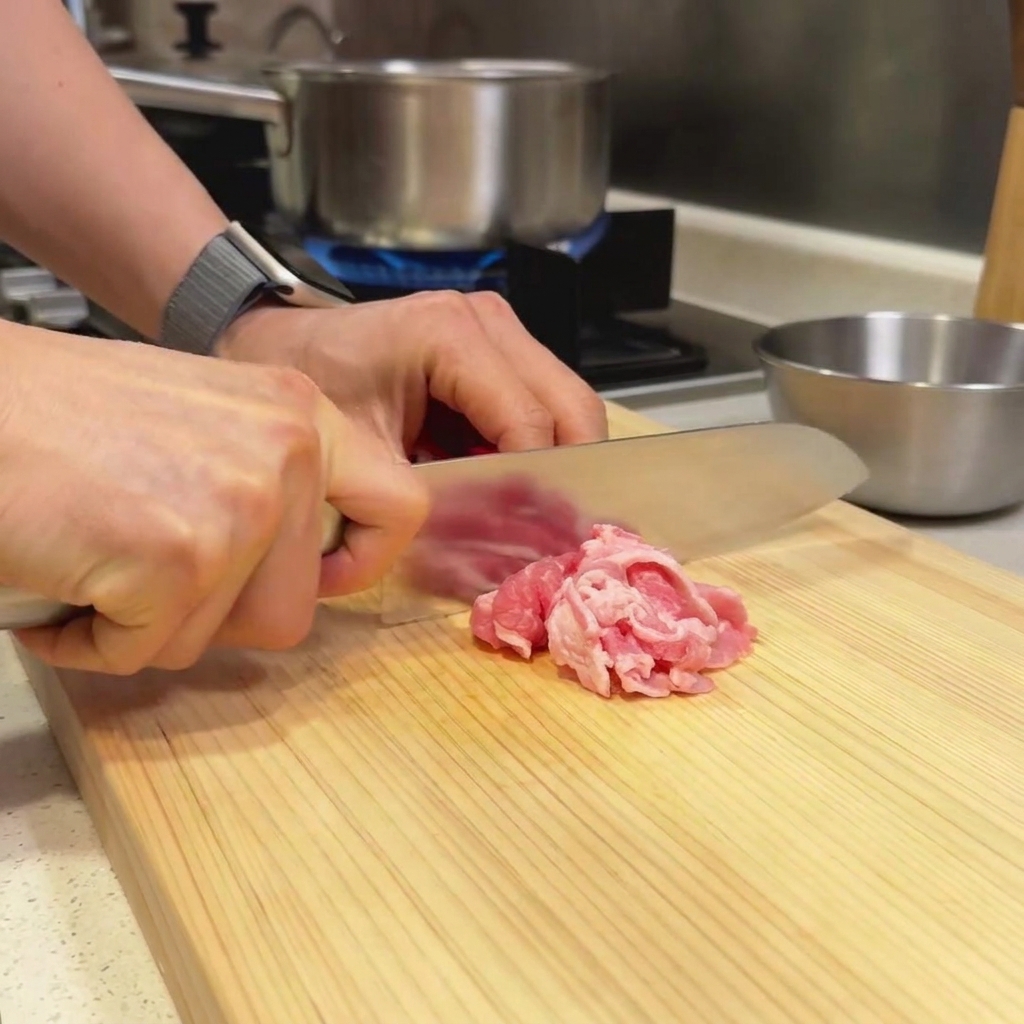 Sottili fette di manzo su un tagliere di legno mentre vengono preparate con un coltello da cucina.