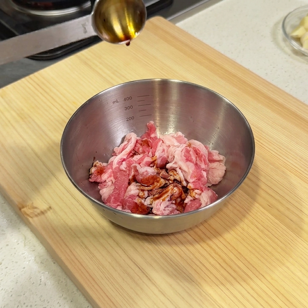 Salsa di soia versata da un cucchiaio dosatore in una ciotola dacciaio piena di fette di manzo crudo.