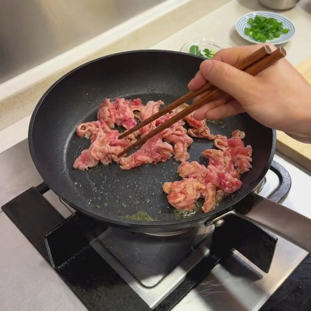 Fette di manzo marinate cotte in una padella nera usando bacchette di legno.
