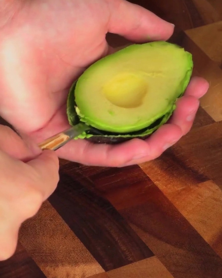 Una persona usa un cucchiaio per estrarre la polpa verde da mezzo avocado.