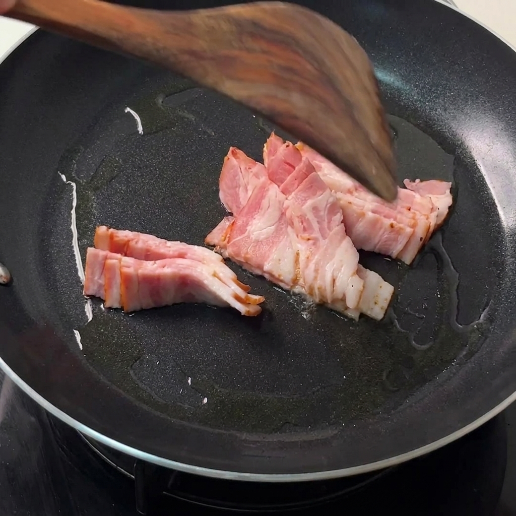 Strisce di pancetta che friggono in una padella nera con una spatola di legno che le gira.