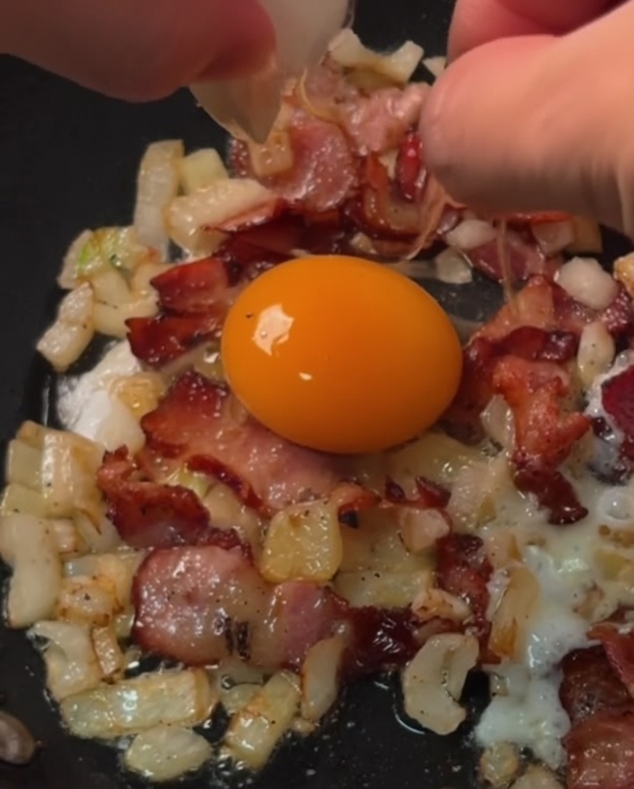 Uova fresche appena rotte nei singoli anelli di pancetta e cipolla in cottura in una padella.