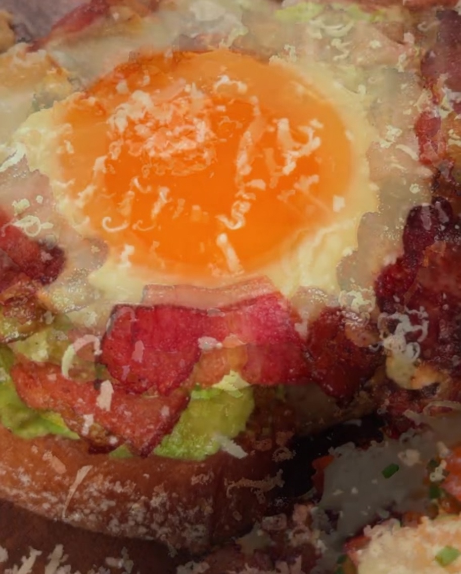 Parmigiano grattugiato spolverato sopra un panino aperto con avocado e uovo appena completato.