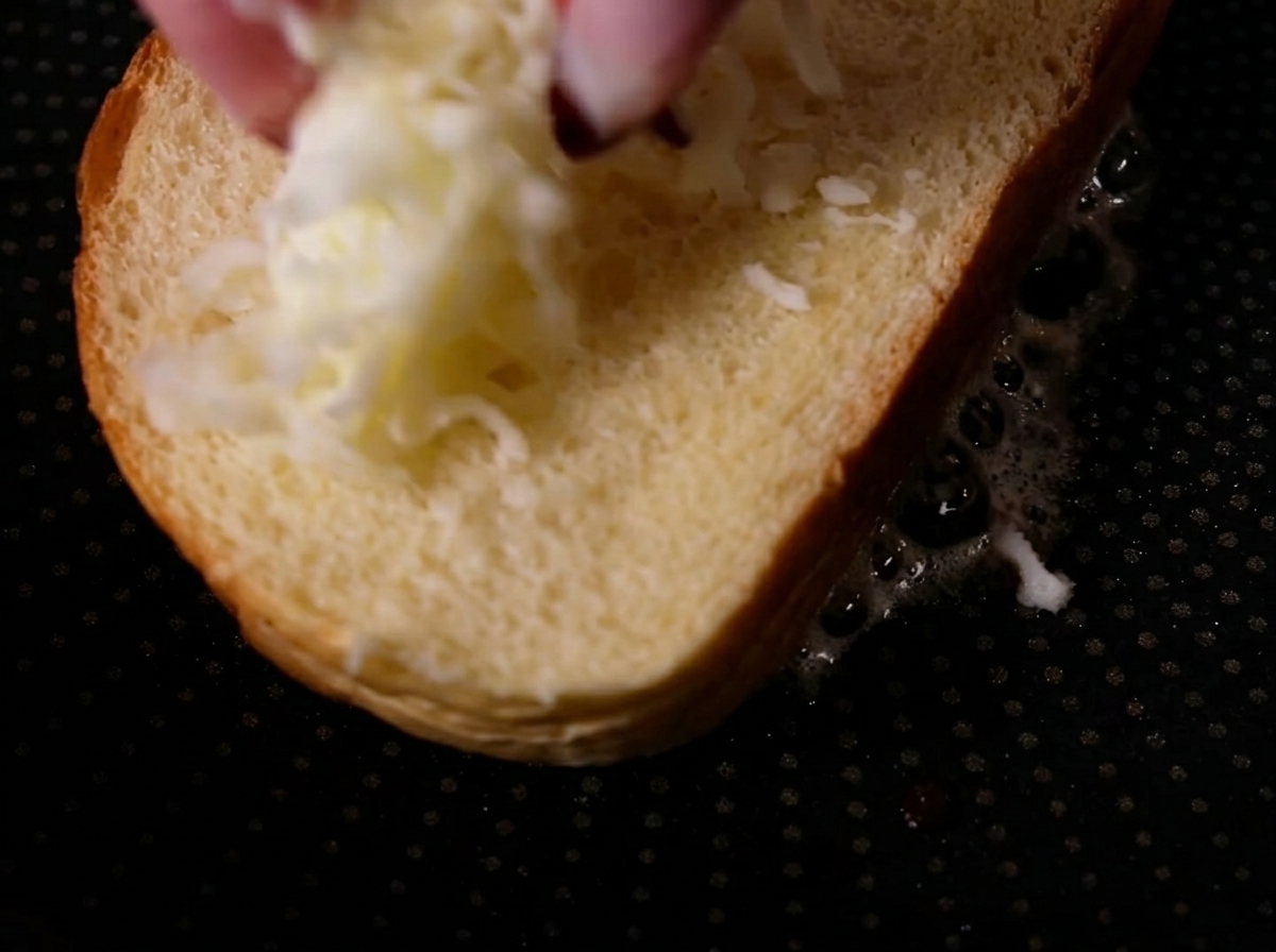 Dita che lasciano cadere mozzarella grattugiata su una semplice fetta di pane in una padella calda.