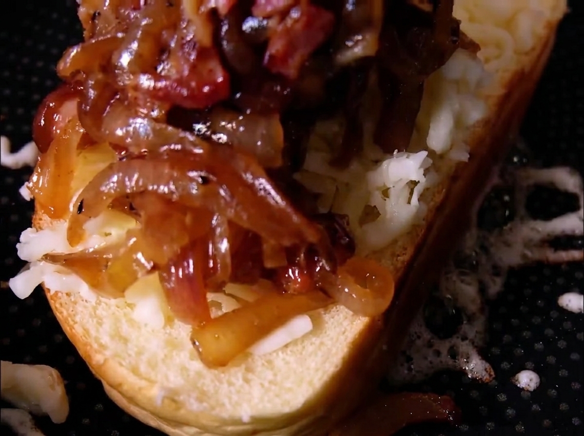 Un generoso mucchietto di cipolle caramellate e pezzi di bacon adagiati sopra il formaggio grattugiato su una fetta di pane.