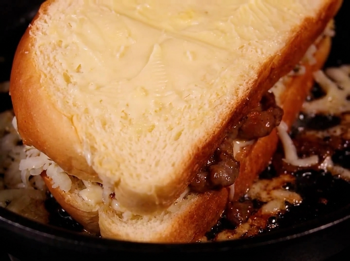Un panino tostato e dorato che viene capovolto in una padella per friggere.