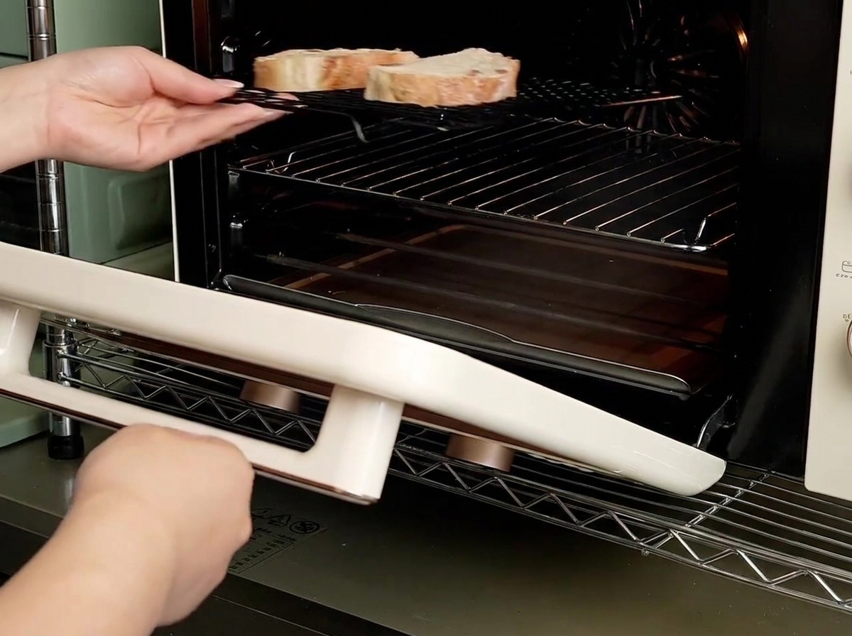 Mani che fanno scorrere una griglia con due fette di pane allinterno di un piccolo forno da banco.
