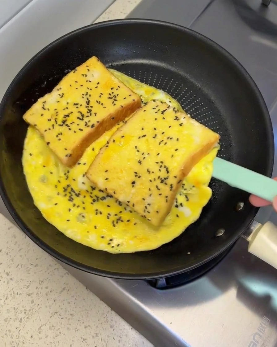 Una spatola in silicone che solleva e capovolge una grande frittata con due fette di pane in padella.