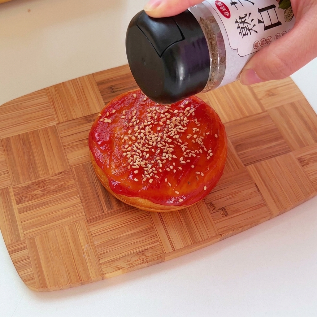 Primo piano di ketchup applicato sulla parte superiore di un panino tondo salato con semi di sesamo.