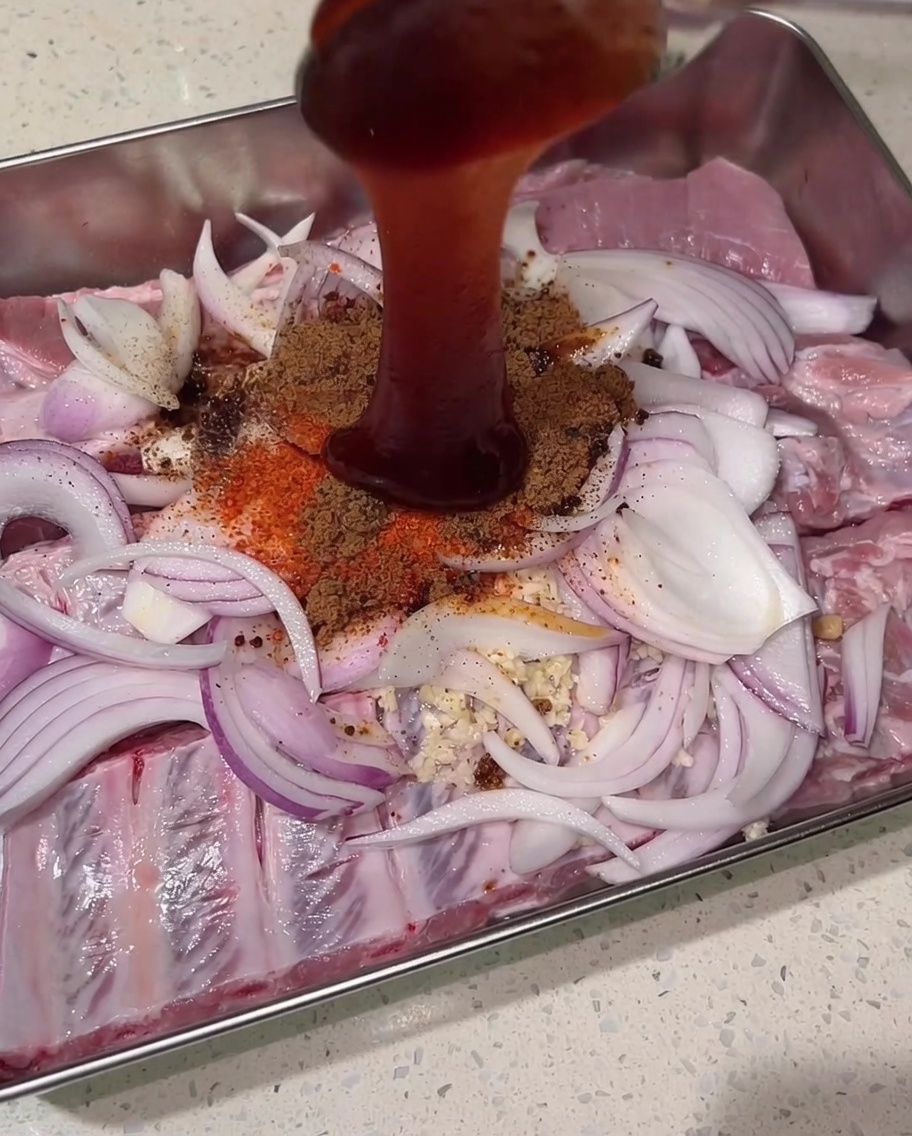 Densa salsa char siu rossa versata dallalto sul mix di spezie secche, costine crude e cipolle.