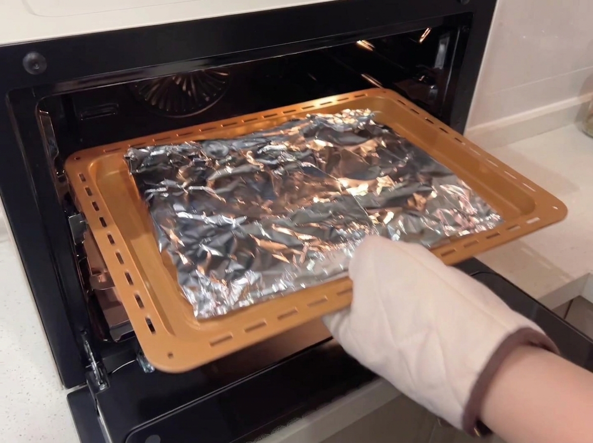 Una persona con guanti da forno inserisce la teglia con le costine avvolte nellalluminio in un forno ventilato.
