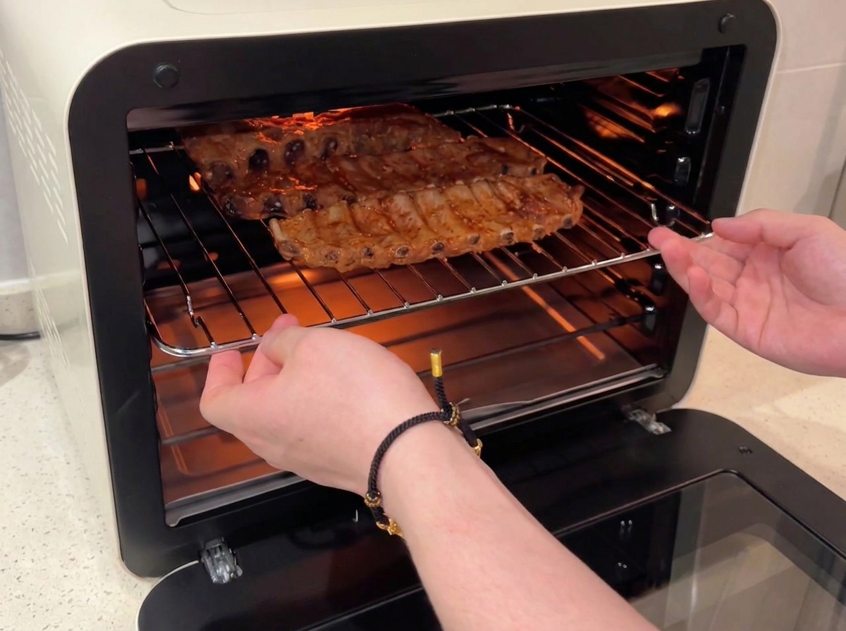 Mani che inseriscono una griglia con le costine glassate al miele nuovamente nel forno acceso.
