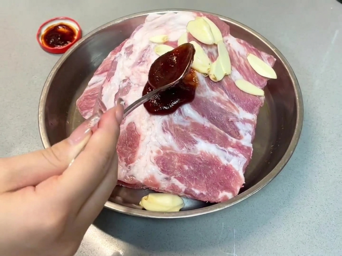 Un cucchiaio di salsa char siu scura versata sulle costine di maiale in una teglia di metallo.