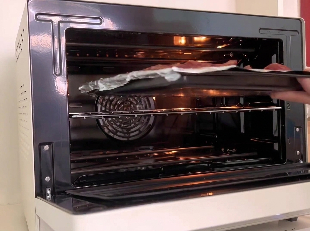 Una teglia con le costine viene fatta scivolare nel ripiano centrale di un forno bianco acceso.