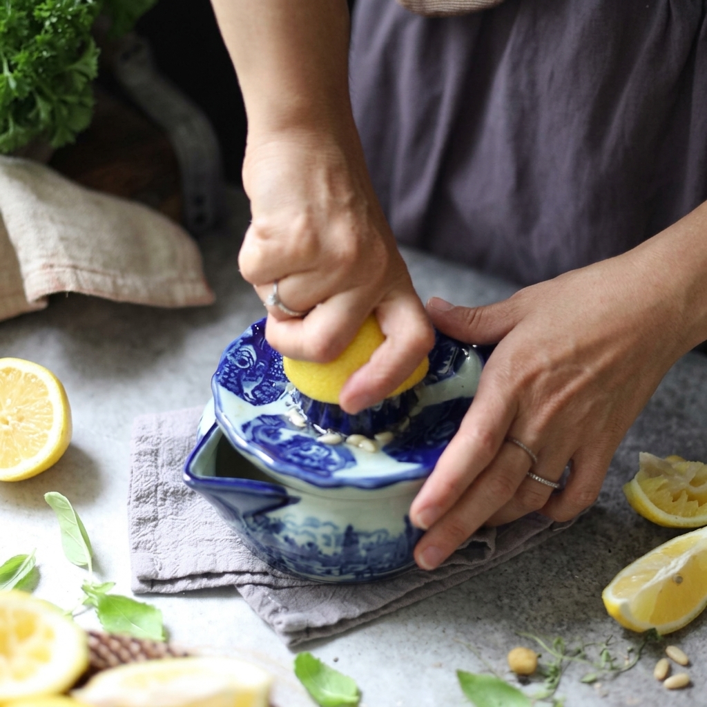 Mani che premono e ruotano mezzo limone su uno spremiagrumi manuale in ceramica blu e bianca.