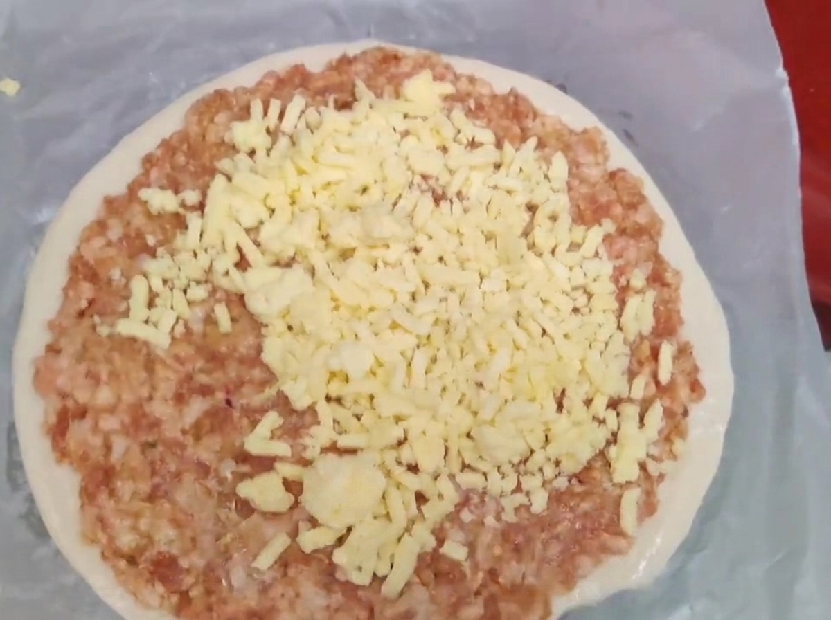 Formaggio giallo grattugiato accumulato sopra uno strato di carne macinata cruda in un pancake.