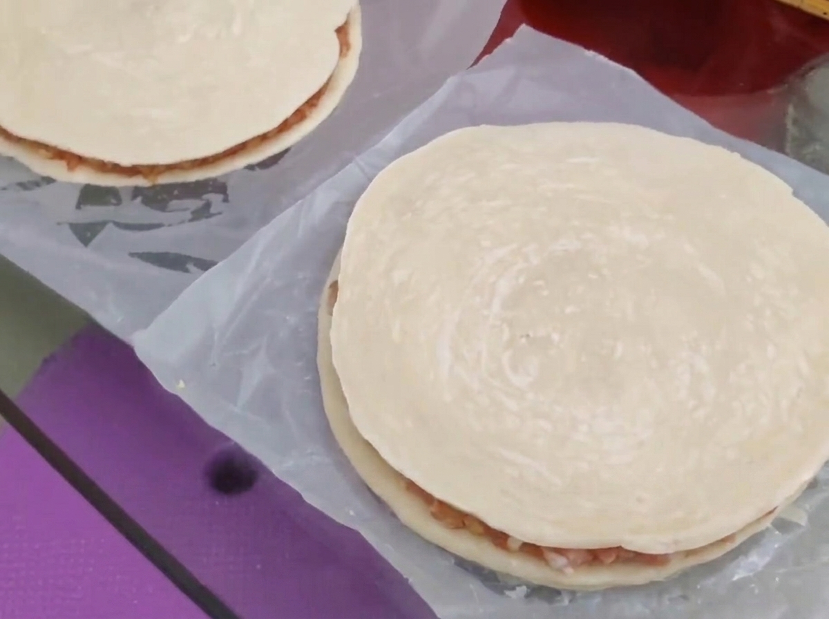 Un secondo pancake rotondo posizionato sopra il ripieno di carne e formaggio per formare una torta chiusa.