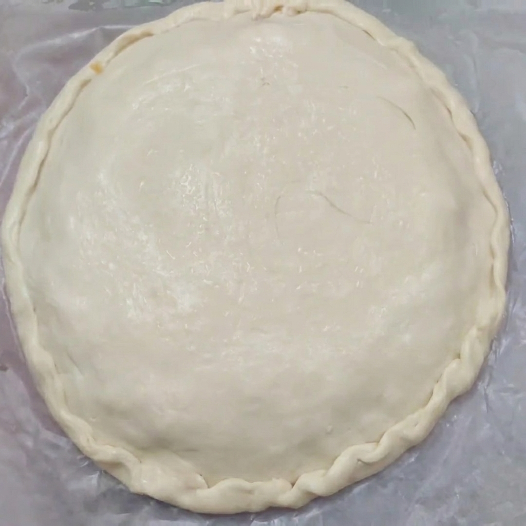 Primo piano di una torta cruda con bordi rifiniti artisticamente che sigillano la pasta superiore e inferiore.