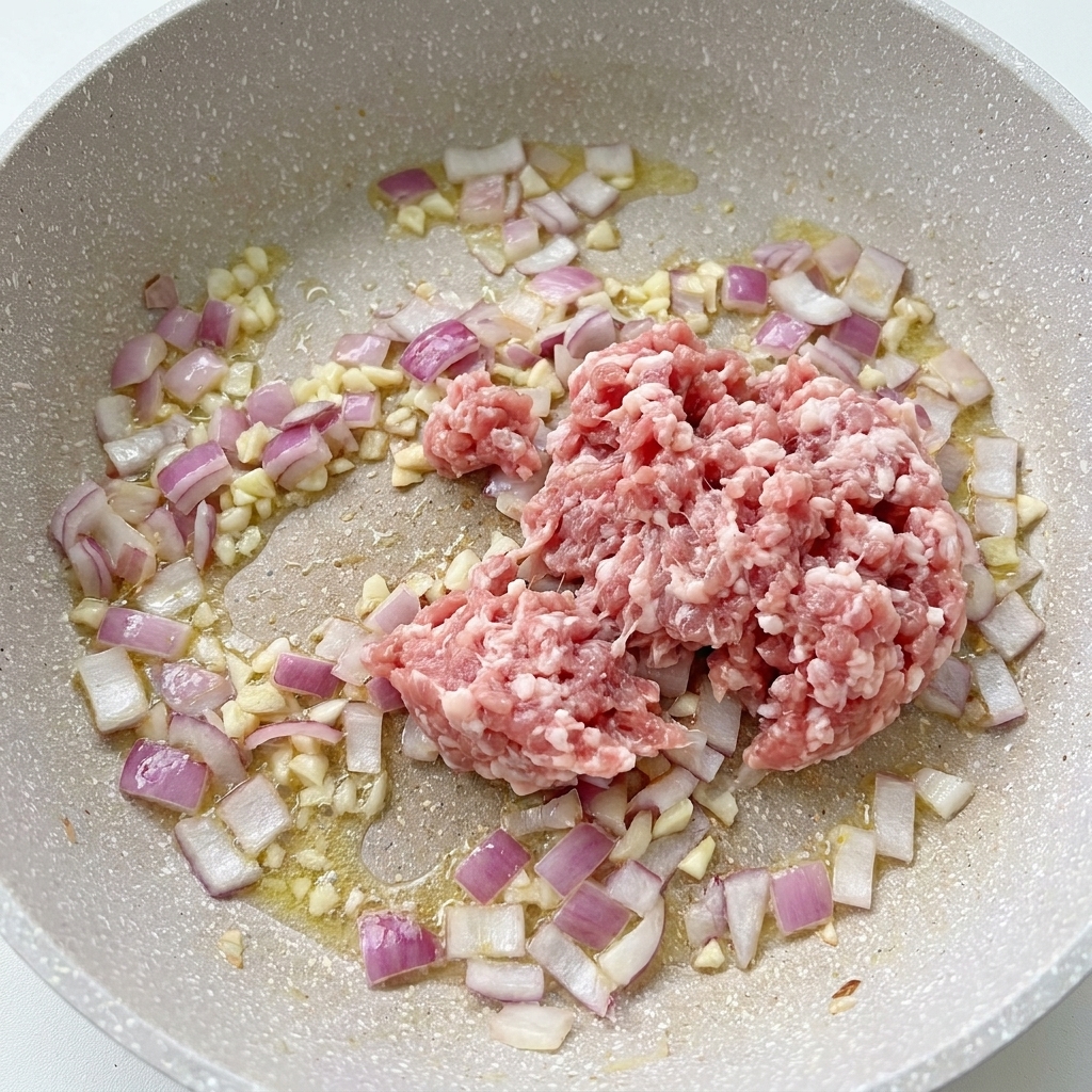 Maiale macinato crudo in padella insieme a cipolle in cottura e aglio tritato.