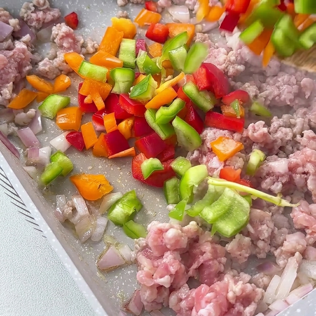 Peperoni misti a dadini rossi, gialli e verdi aggiunti nella padella con il composto di carne.