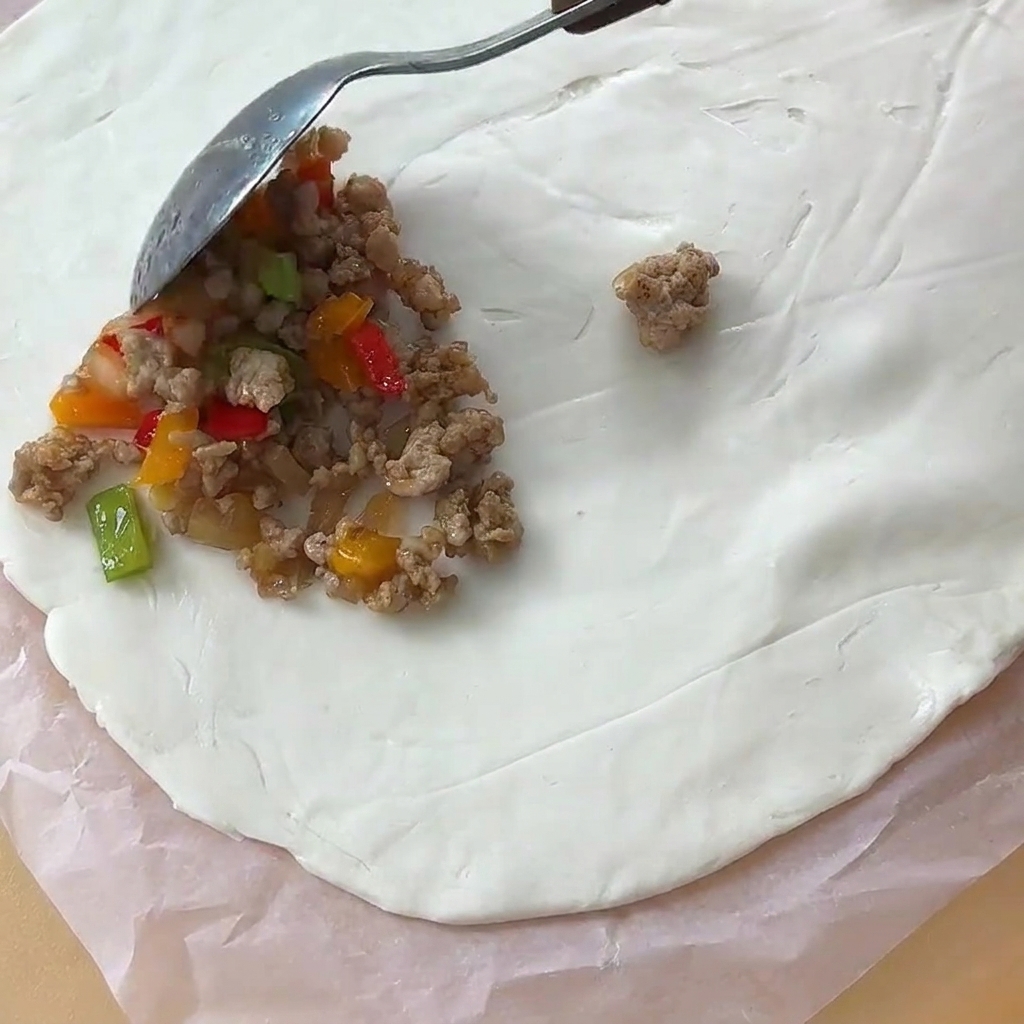 Un cucchiaio di ripieno di carne cotto posizionato al centro di un foglio circolare di pasta di pane piatto su carta da forno.