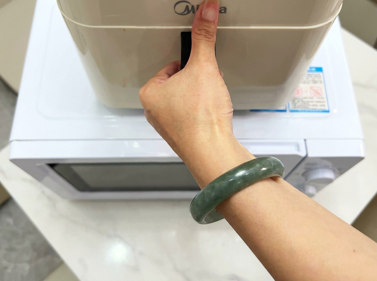 Una mano che regge la maniglia di un elettrodomestico da cucina moderno posizionato su una superficie bianca.