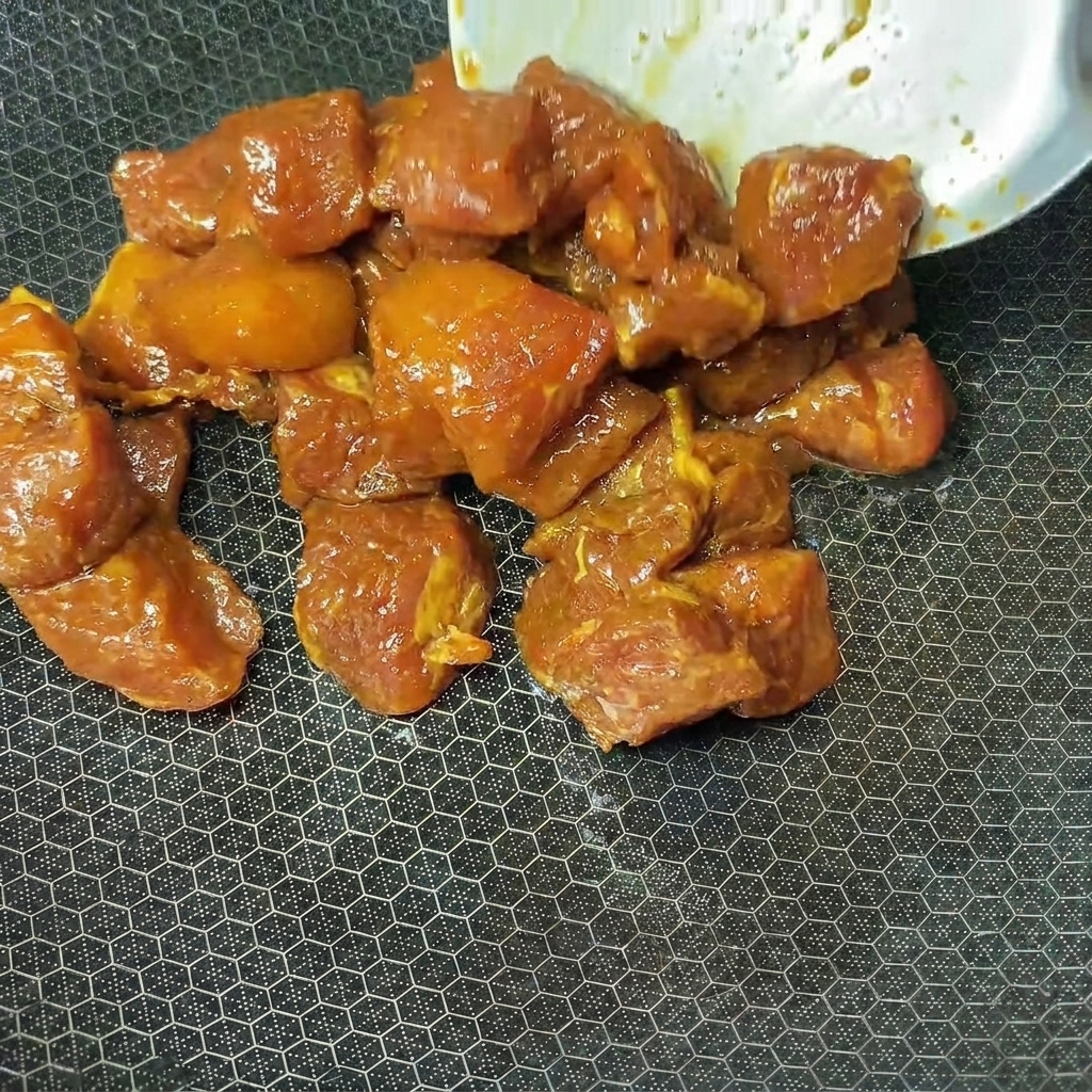 Cubetti di maiale marinati inseriti in un wok caldo per la cottura.